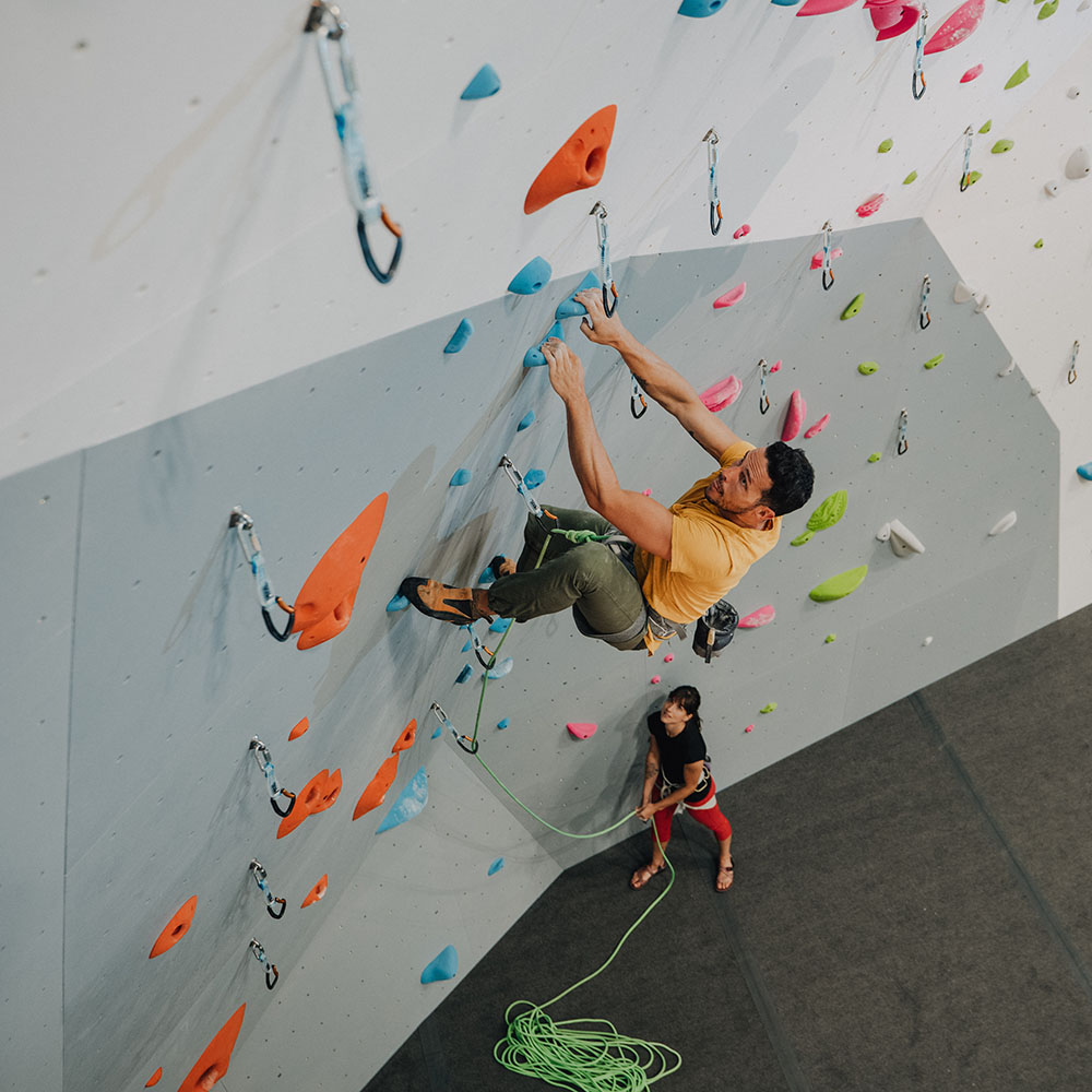 Man lead climbs while a woman belays him.